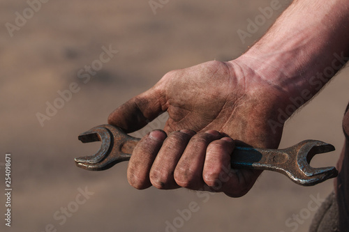 Dirty hands mechanics after the repair of equipment. Spanner wrench in hand. Can be used as a poster or background for design.