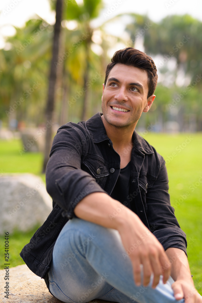 Happy young Hispanic man sitting and thinking at the park Happy young Hispanic man sitting and thinking at the park
