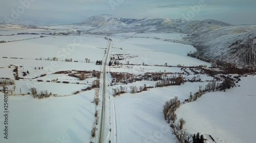 Small highway road crossing through a snowy field outside of Cokeville, Wyoming. Static drone, looking over road, mountains in background. photo