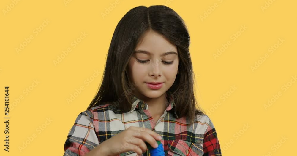 Close up of the Caucasian pretty small schoolgirl with a long hair blowing soap bubbles on the yellow background. Close up of the Caucasian pretty small schoolgirl with a long hair blowing soap bubbles on the yellow background.