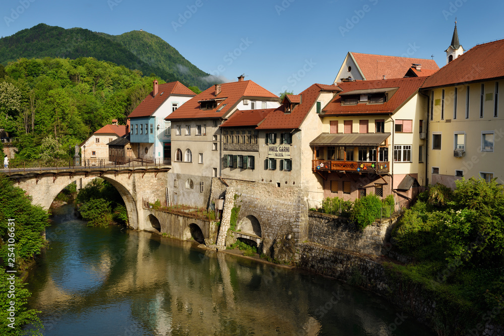 Stone Capuchin bridge and historic houses reflected in the Selca Sora river in Skofja Loka village Slovenia