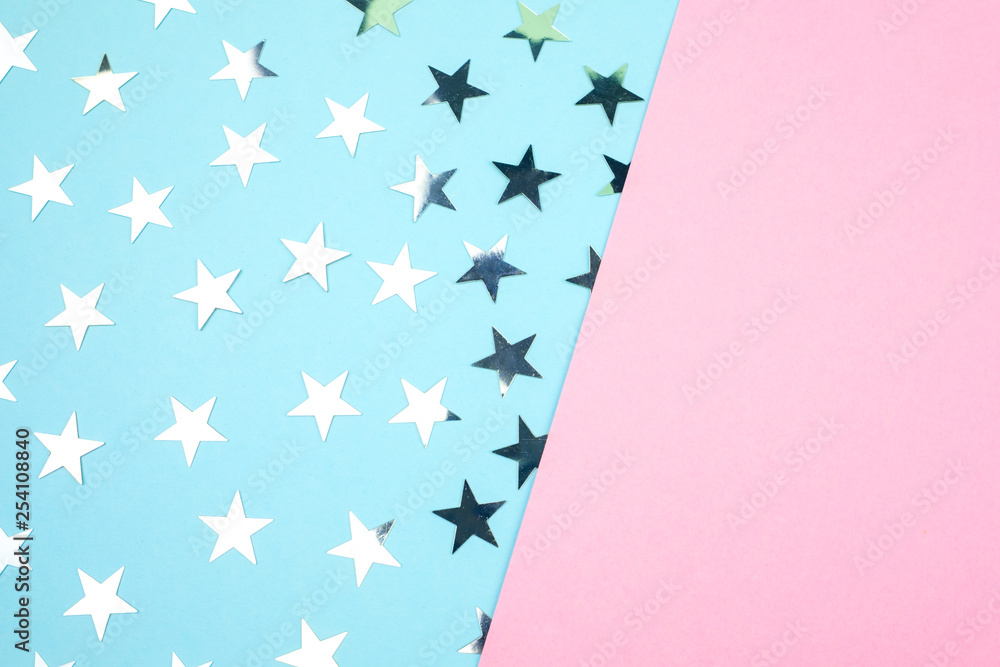 The background is divided into two parts, pink is empty on it a place for text, silver star shape confetti is laid out on blue parts. Festive concept. The background is divided into two parts, pink is empty on it a place for text, silver star shape confetti is laid out on blue parts. Festive concept.