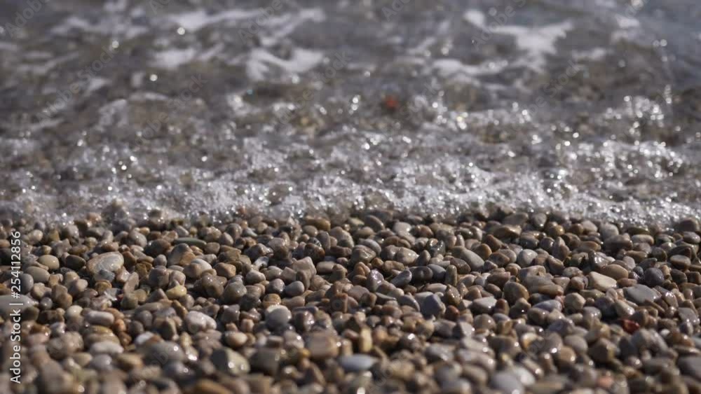 Waves washing the pebble beach. Close Up View of Crashing Water Waves on Pebbles Rocks Waves washing the pebble beach. Close Up View of Crashing Water Waves on Pebbles Rocks
