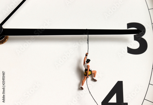 A miniature climber hanging by a rope on a black watch needle. photo