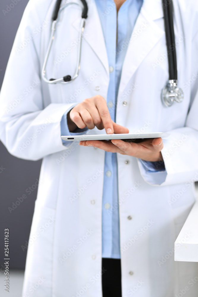 Female physician using digital tablet while standing near reception desk at clinic or emergency hospital. Unknown doctor woman at work. Medicine concept Female physician using digital tablet while standing near reception desk at clinic or emergency hospital. Unknown doctor woman at work. Medicine concept