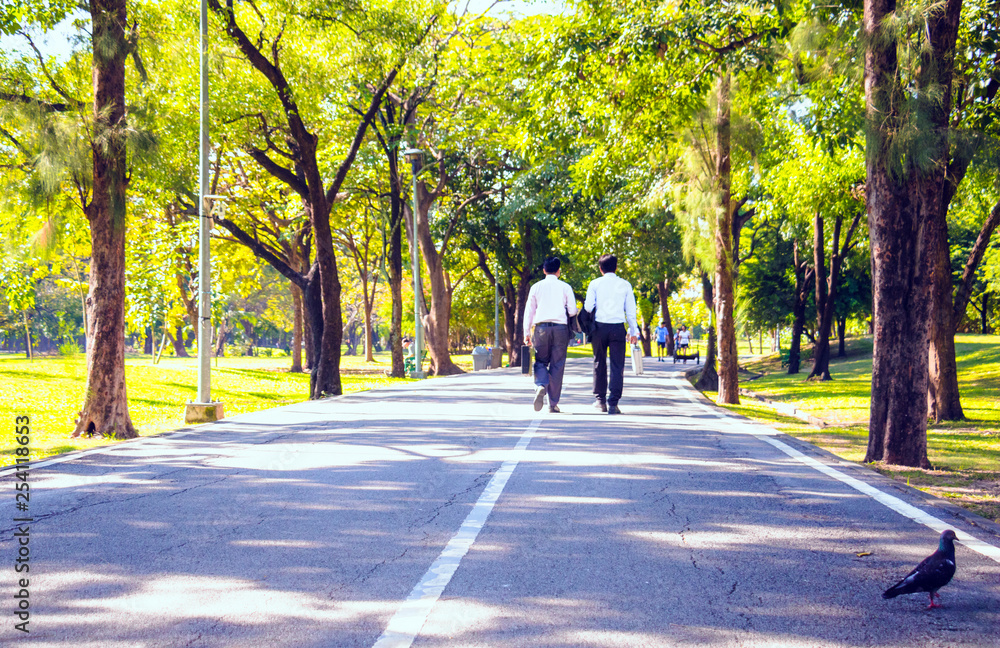 Businessman, They are walking on road in park. They are talking  business. He is drinking coffee and His friend holding business bag. Photo concept business and relax time.