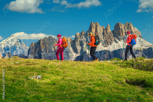 Happy woman hikers with backpacks walking in mountains, Dolomites, Italy