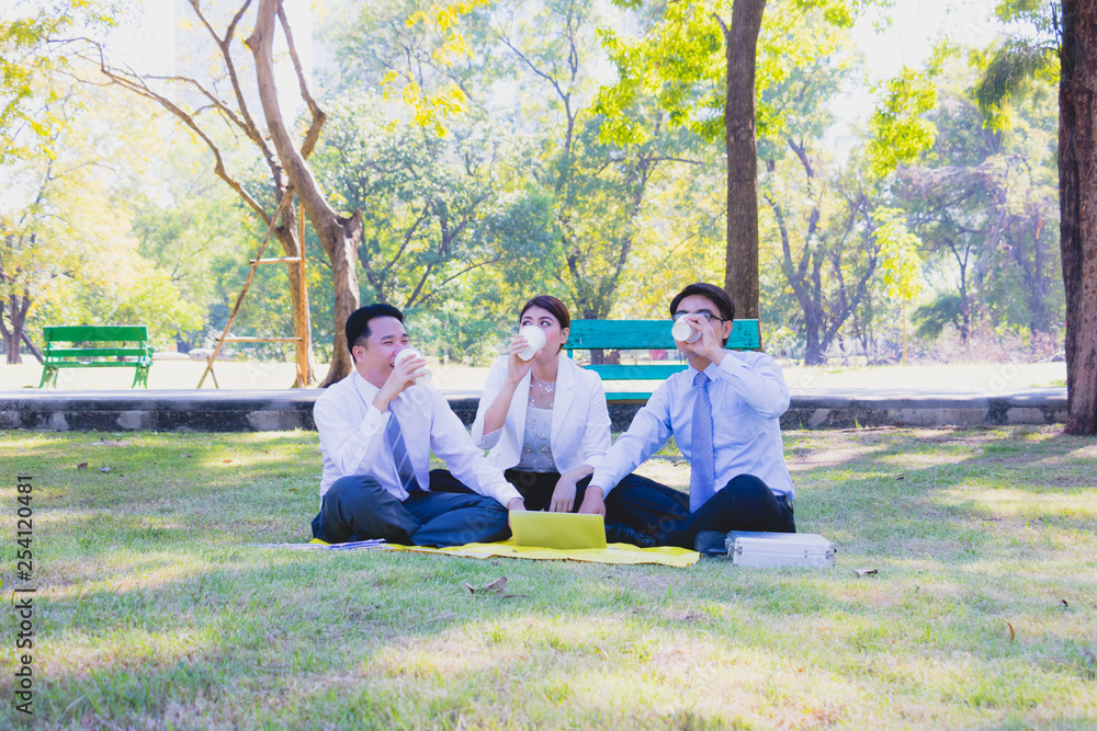 Business team work. They are talking in the park. they are talking about business and on the floor had a notebook and a glass of coffee.Photo concept business and relax time. Business team work. They are talking in the park. they are talking about business and on the floor had a notebook and a glass of coffee.Photo concept business and relax time.