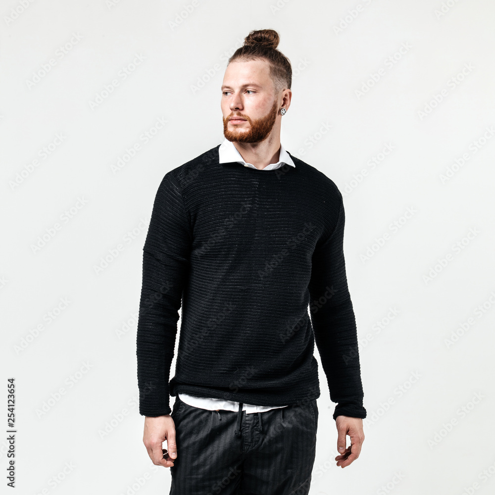 Stylish man with beard and bun hairstyle wearing a black jumper over a white shirt and trousers poses in the studio on the white background Stylish man with beard and bun hairstyle wearing a black jumper over a white shirt and trousers poses in the studio on the white background