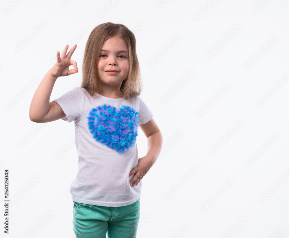 Close up shot of little positive girl with long fair hair looking at camera artistically and shows ok-gesture. The portrait is made on a white background. Close up shot of little positive girl with long fair hair looking at camera artistically and shows ok-gesture. The portrait is made on a white background.