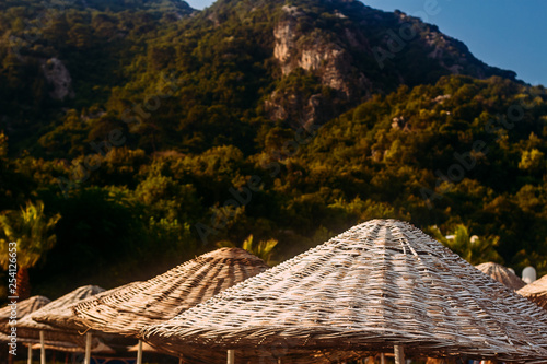wicker bamboo umbrellas on ha beach background of mountains © Alyona