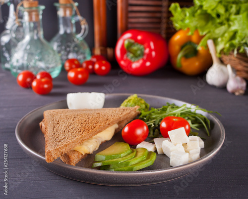 Sandwich with turkey breast, cheese, lettuce, arugula, tomatoes, feta, avocado and onion on a plate