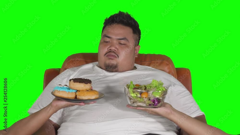 Overweight man looks confused to choose donuts or vegetables salad. Shot in 4k resolution with green screen background Overweight man looks confused to choose donuts or vegetables salad. Shot in 4k resolution with green screen background