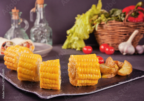 Slices of Corn Cob on a black plate with vegetables on the background