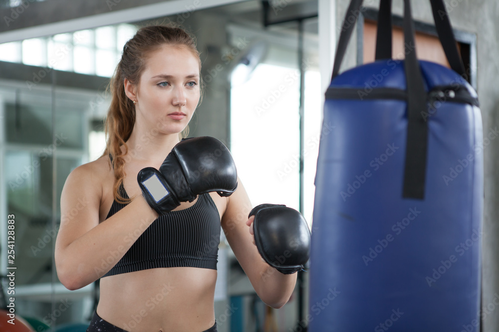 young fitness girl doing exercise hitting punching bag at a boxing studio gym.woman boxer in sportswear working out with gloves