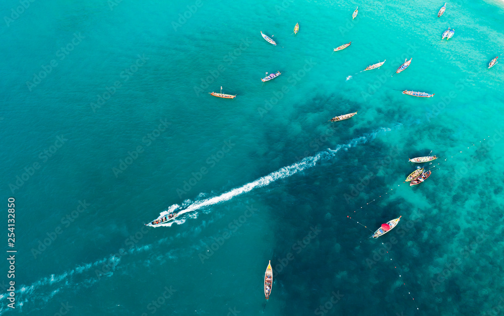 View from above, stunning aerial view of a large group of traditional longtail boats floating on a turquoise and clear sea that bathes the tropical Freedom beach in Phuket, Thailand.