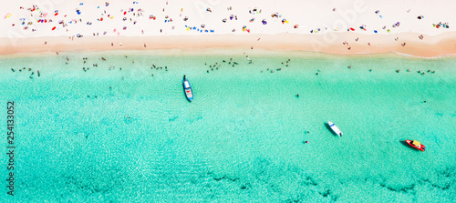 View from above, stunning aerial view of a beautiful tropical beach with white sand and turquoise clear water, long-tail boat and people sunbathing, Surin beach, Phuket, Thailand.