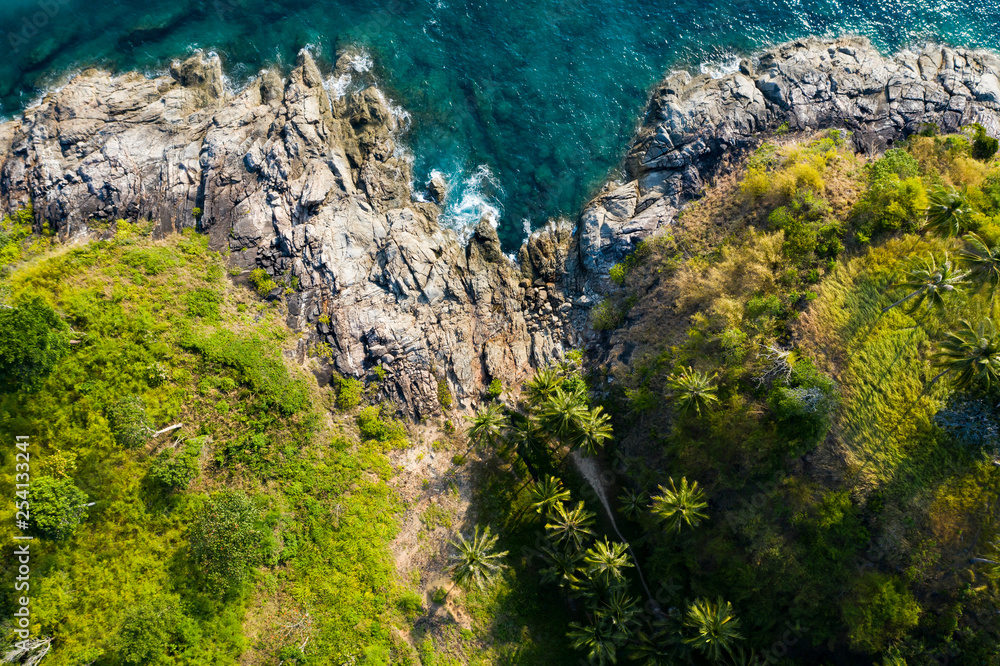 View from above, stunning aerial view of a beautiful tropical rocky coast with palm trees bathed by a turquoise and clear water, Freedom Beach, Phuket, Thailand.