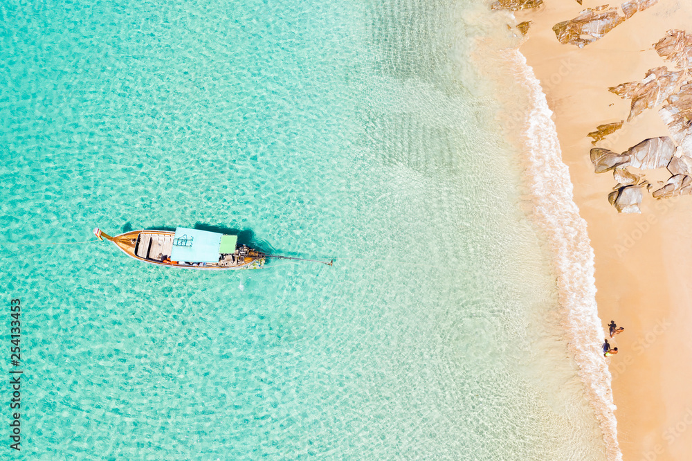 View from above, stunning aerial view of two people walking on a beautiful tropical beach with white sand, turquoise clear water and a traditional long-tail boat. Banana beach, Phuket, Thailand.