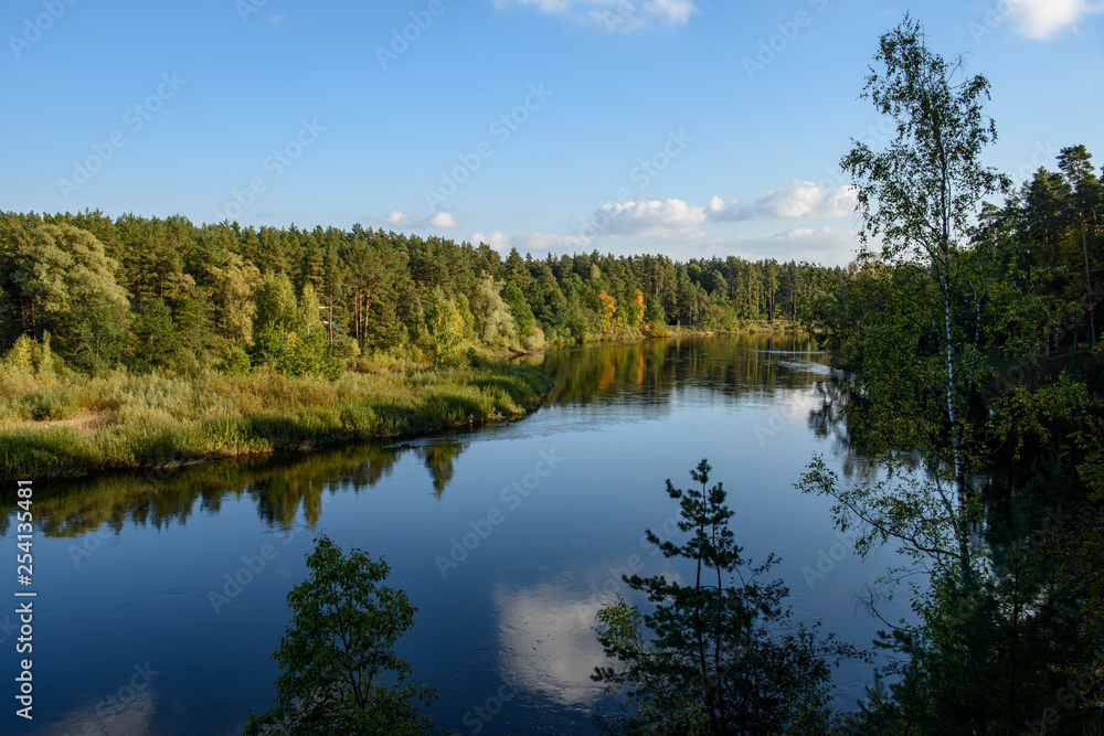 calm lake in bright sun light with reflections of clouds and trees and blue sky calm lake in bright sun light with reflections of clouds and trees and blue sky