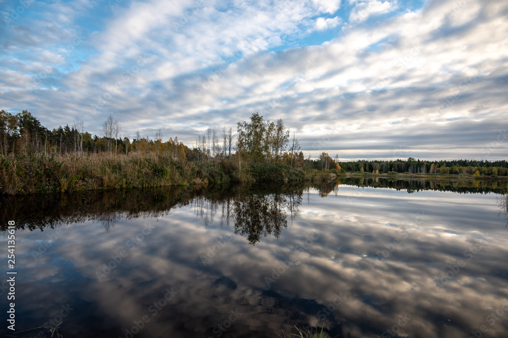 calm lake in bright sun light with reflections of clouds and trees and blue sky calm lake in bright sun light with reflections of clouds and trees and blue sky
