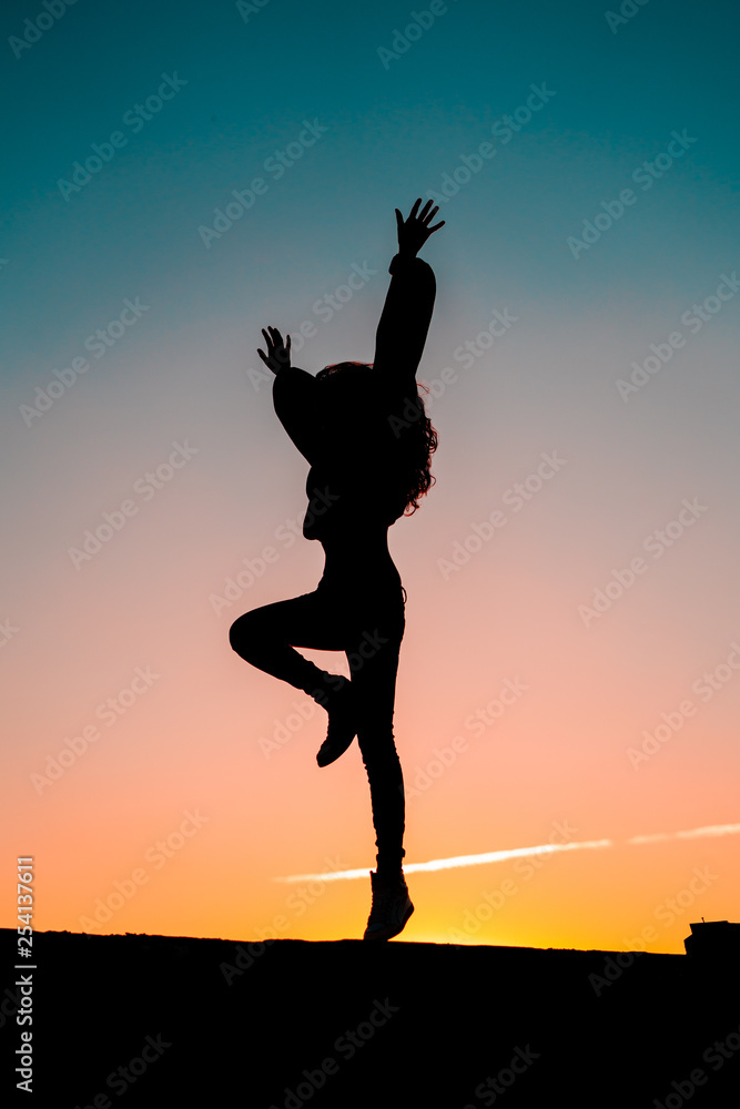 Silhouette of an attractive young woman jumping on wall during sunset. Energy concept.