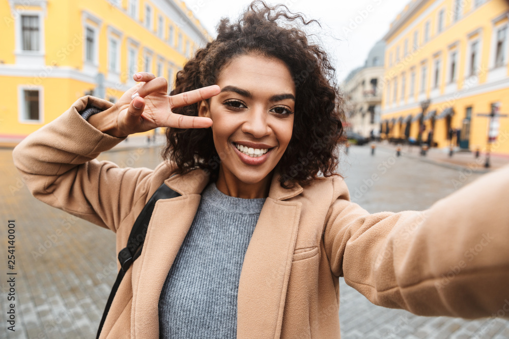 Fototapeta premium Cheerful young african woman wearing coat walking