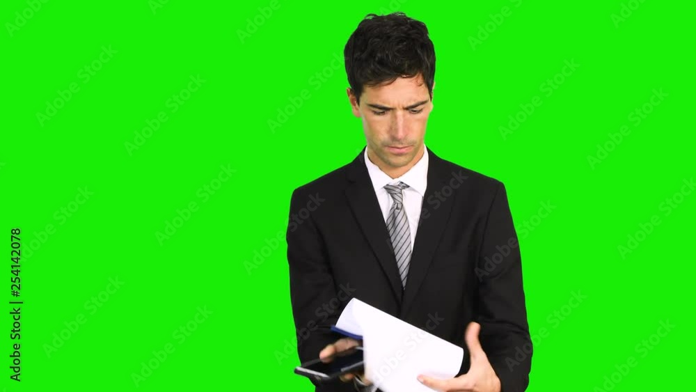 Young businessman talking on mobile phone while reading on clipboard isolated against green screen background Young businessman talking on mobile phone while reading on clipboard isolated against green screen background