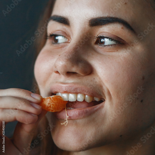 Cute girl playfully eating sweet tangerine. Close up