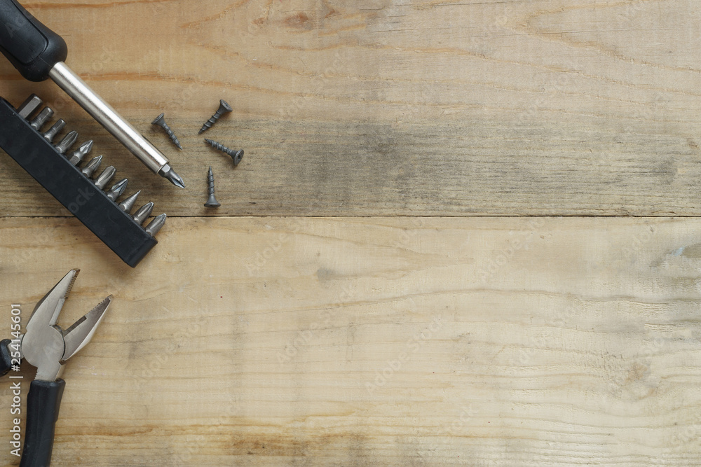 Screwdriver, pliers, screws on wooden background