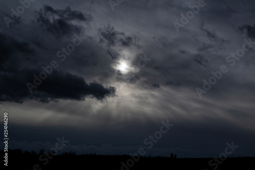 Cloudy sky with sun. Black silhouette of horizon. Underexposed and dark cloudy weather