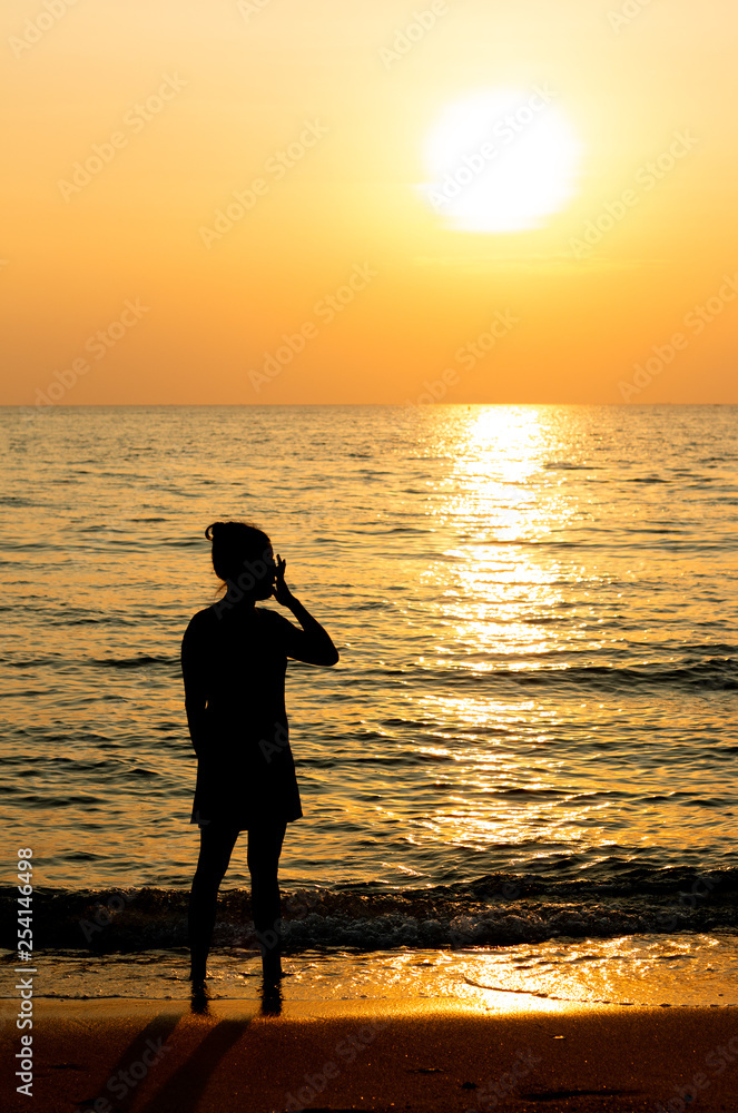 1 woman is standing at the beach when sun set.silhouette