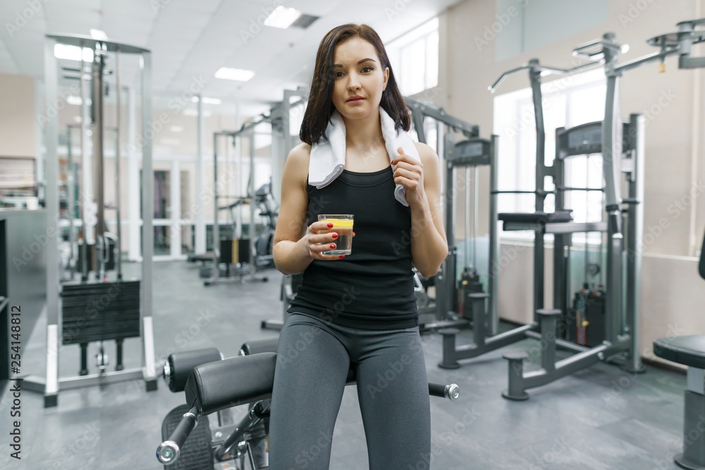 Portrait of young beautiful fitness woman in sportswear with towel, with glass of water and lemon, after fitness classes drinking water in gym. Healthy lifestyle and nutrition Portrait of young beautiful fitness woman in sportswear with towel, with glass of water and lemon, after fitness classes drinking water in gym. Healthy lifestyle and nutrition