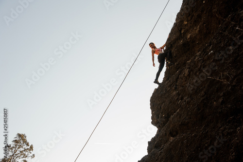 Girl equipped with a rope climbing on the sloping rock and looking down