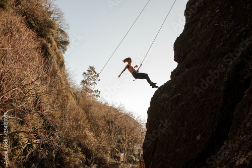 Sporty girl equipped with a rope abseiling on the sloping rock