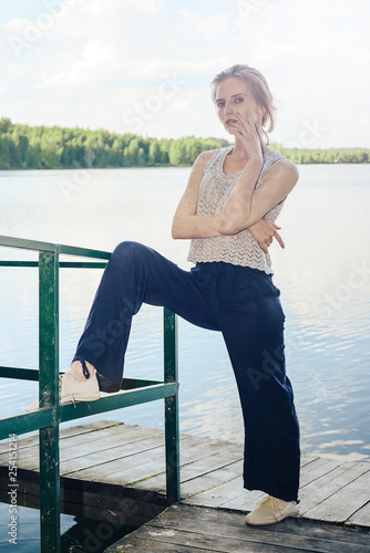 Attractive girl standing on the pier in the Park by the lake, putting one foot on the railing. The concept of spring and summer holidays in the Park, in nature. © indigo_nifght
