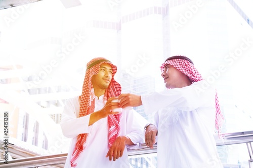 Two young Arabian businessman are having drink and friendly conversation on modern white building background