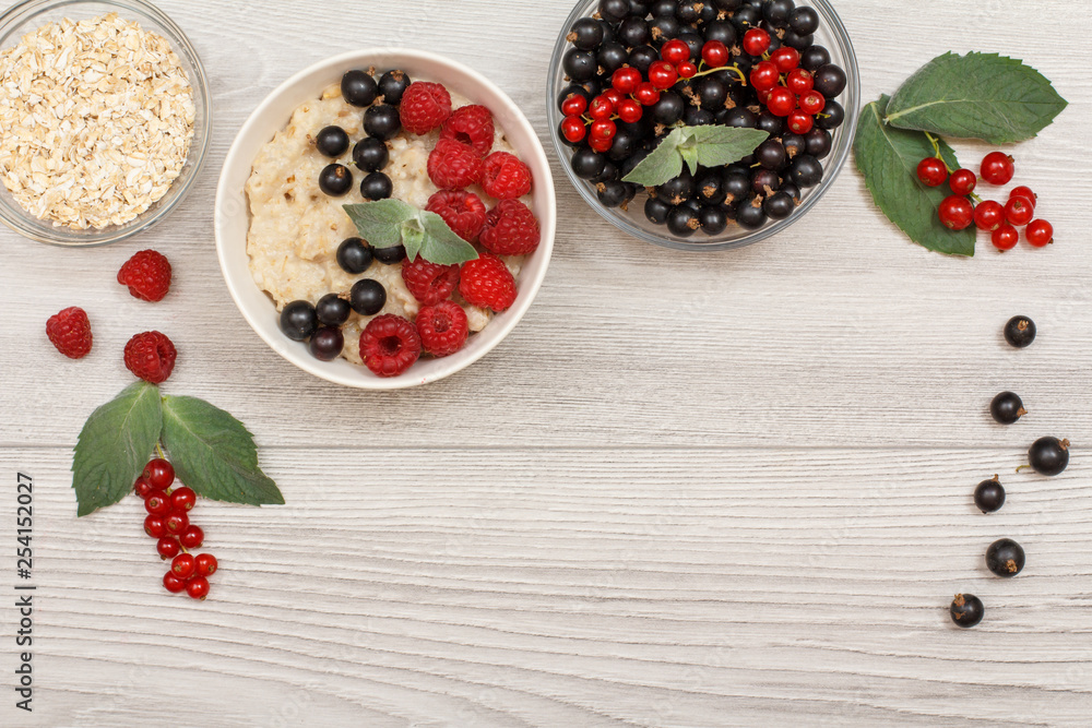 Oatmeal porridge in porcelain bowl with currant berries and raspberries, decorated with mint leaves Oatmeal porridge in porcelain bowl with currant berries and raspberries, decorated with mint leaves