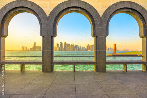 Modern skyscrapers of Doha West Bay skyline at sunset light through arches of museum located along Corniche in Qatari capital. Doha in Qatar. Middle East, Arabian Peninsula in Persian Gulf.