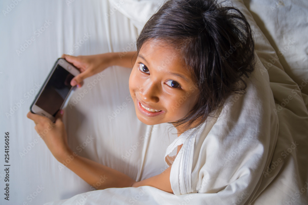 happy and beautiful 7 years old child having fun playing internet game with mobile phone lying on bed cheerful and excited in young girl and technology concept happy and beautiful 7 years old child having fun playing internet game with mobile phone lying on bed cheerful and excited in young girl and technology concept