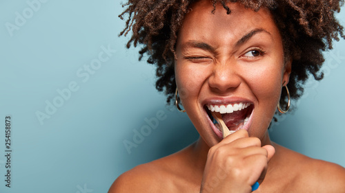 Fotografia Close up shot of happy joyful funny dark skinned young woman has Afro hair brush