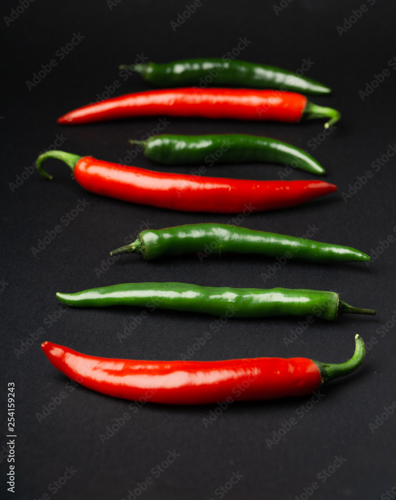 Green and red chili peppers on black background. Hot spicy food symbol.