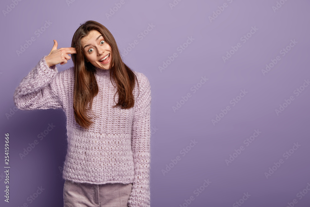 Pretty funny woman shoots in temple, tilts head, foolishes and shows suicide gesture, has happy facial expression, stands over purple wall with free space for your advertisement. Body language Pretty funny woman shoots in temple, tilts head, foolishes and shows suicide gesture, has happy facial expression, stands over purple wall with free space for your advertisement. Body language