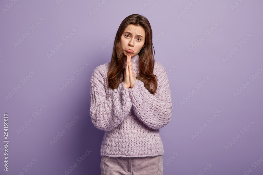 Sad begging woman has pleading expression, asks for fortune or apologize, purses lips, keeps plam pressed together, begs for apology and giving chance, dressed in casual winter outfit, models indoor Sad begging woman has pleading expression, asks for fortune or apologize, purses lips, keeps plam pressed together, begs for apology and giving chance, dressed in casual winter outfit, models indoor