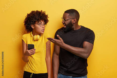 Irritated angry black father reproaches daughter of constant listening music in headphones and addiction to modern technologies, asks for help, gestures while argues. Give me cellphone please