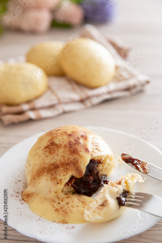 Germknödel oder Hefeklöße mit Pflaumenmusfüllung und Vanillesoße auf weißem Teller und hellem Holzuntergrund