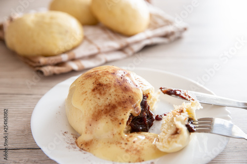 Germknödel oder Hefeklöße mit Pflaumenmusfüllung und Vanillesoße auf weißem Teller und hellem Holzuntergrund