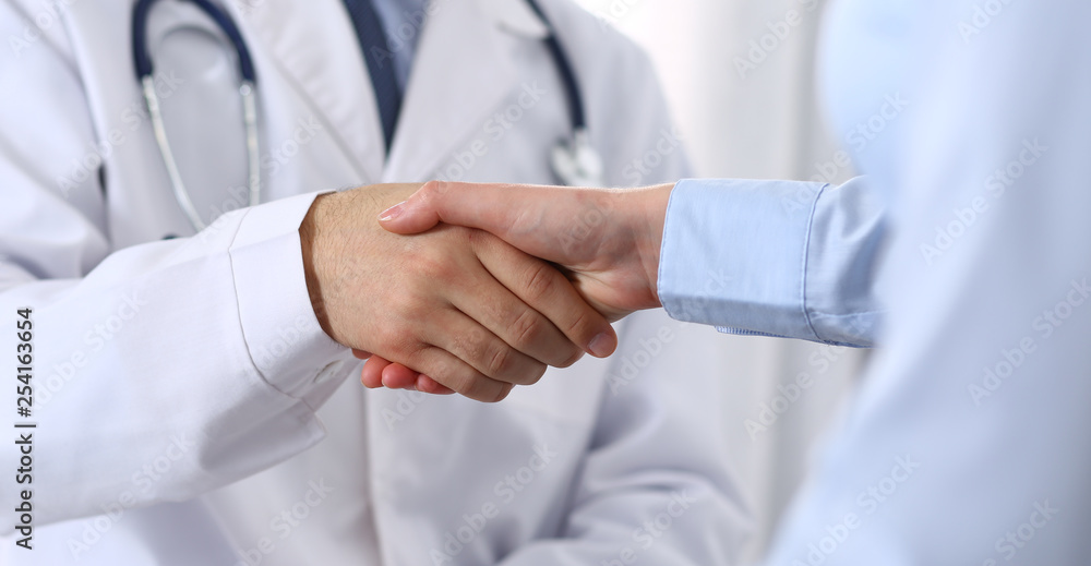 Male doctor and woman patient shaking hands. Partnership in medicine, trust and medical ethics concept Male doctor and woman patient shaking hands. Partnership in medicine, trust and medical ethics concept