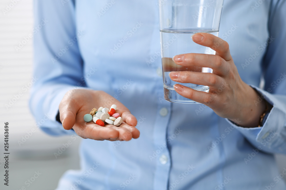 Young unknown woman holding pills and glass of water, closeup of hands. Medicine and healthcare concept Young unknown woman holding pills and glass of water, closeup of hands. Medicine and healthcare concept