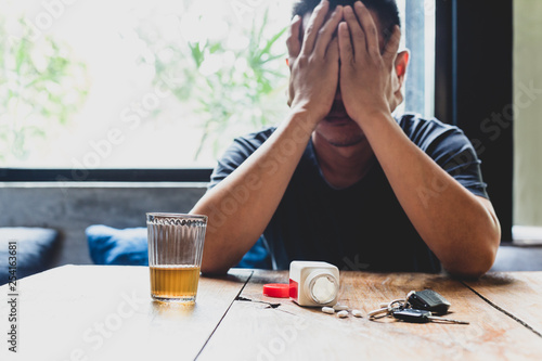 Tablou pe pânză Depression man hand on his face with glass of alcohol and pills on the table